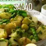 A large bowl of potato salad with peas, sugar snap peas, dill and pickles mixed through it. There is a large jar of dill pickles in the background.