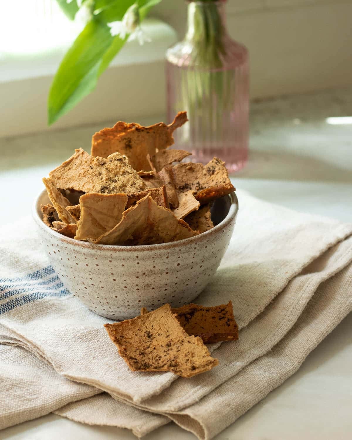 A bowl of tofu crispy crackers with a few spilled next to the bowl.