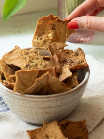 A bowl of tofu crispy crackers with a few spilled next to the bowl.