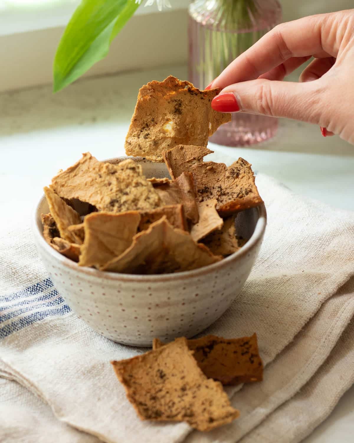 A bowl of tofu crispy crackers with a few spilled next to the bowl.