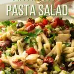 A big bowl of antipasto pasta salad being dressed with balsamic vinaigrette dressing.
