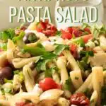 A big bowl of antipasto pasta salad being dressed with balsamic vinaigrette dressing.