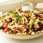 A big bowl of antipasto pasta salad being dressed with balsamic vinaigrette dressing.