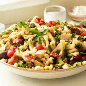 A big bowl of antipasto pasta salad being dressed with balsamic vinaigrette dressing.