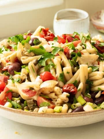 A big bowl of antipasto pasta salad being dressed with balsamic vinaigrette dressing.