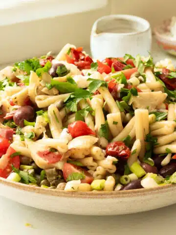 A big bowl of antipasto pasta salad being dressed with balsamic vinaigrette dressing.