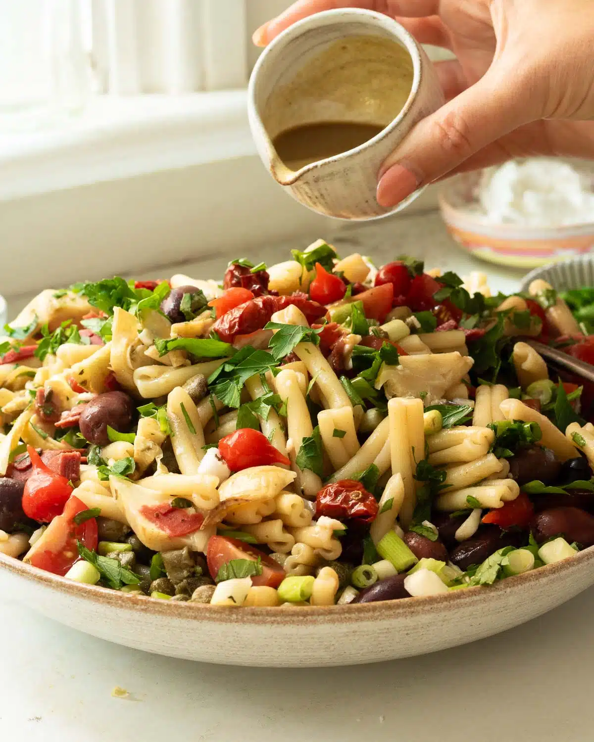 A big bowl of antipasto pasta salad being dressed with balsamic vinaigrette dressing. 