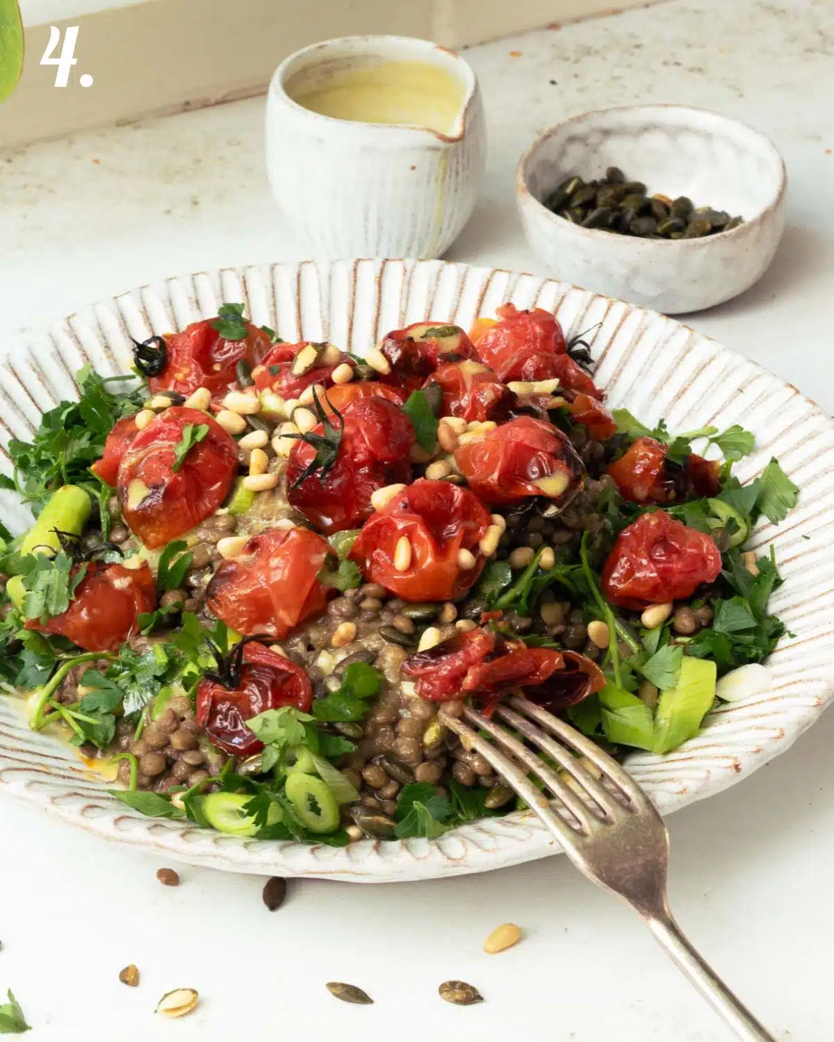 A plate of green lentils topped with seeds, herbs and roasted tomatoes.