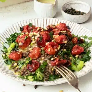 A plate of green lentils topped with seeds, herbs and roasted tomatoes.