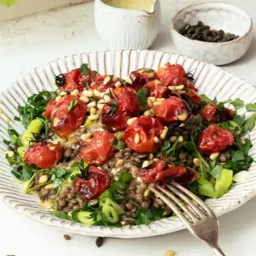 A plate of green lentils topped with seeds, herbs and roasted tomatoes.