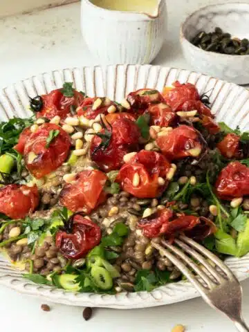 A plate of green lentils topped with seeds, herbs and roasted tomatoes.