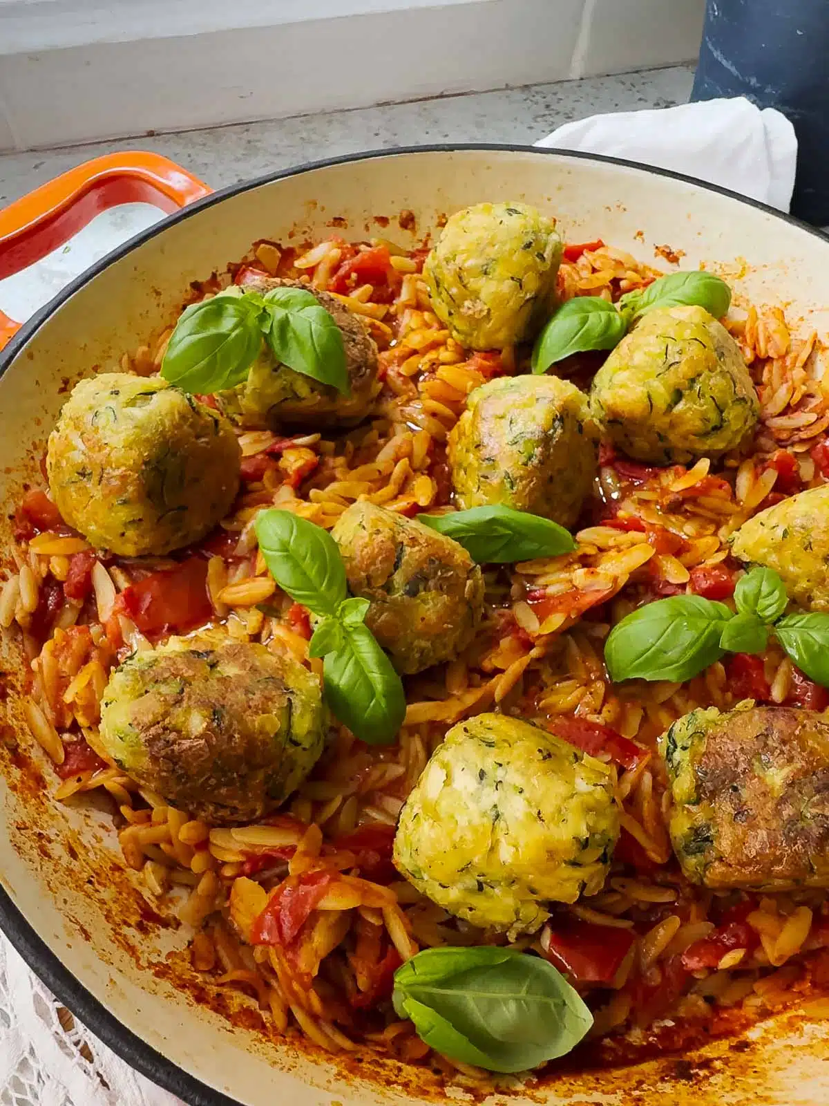 A pan of spicy tomato orzo with tofu meatballs on top with some extra basil sprinkled over.