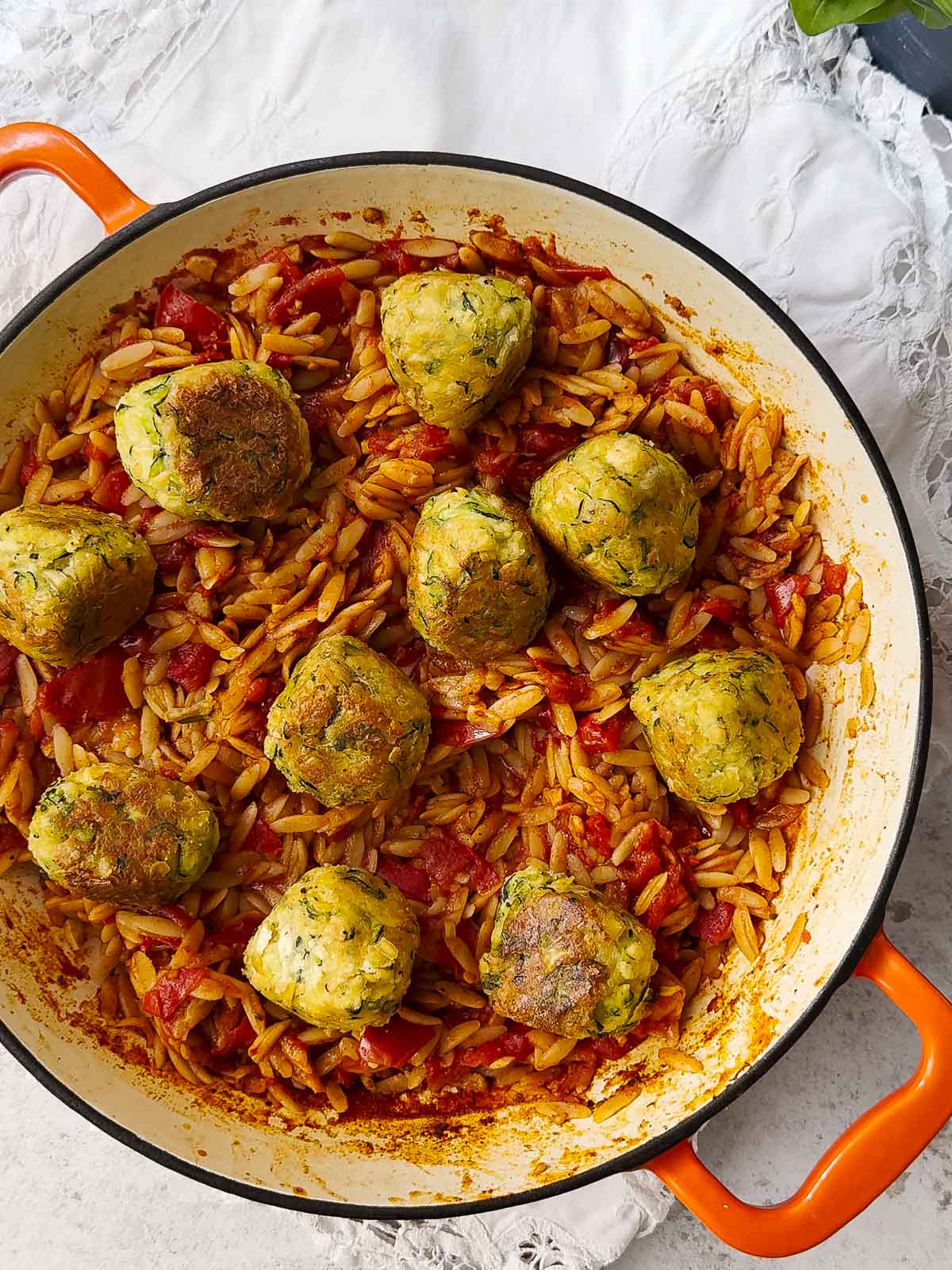A large skillet with orzo pasta cooked in tomato sauce in it. On top of the orzo are tofu and zucchini meatballs .