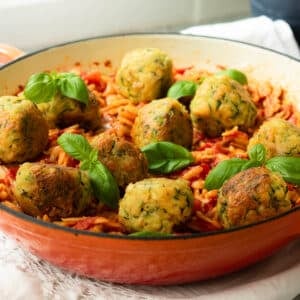 A pan of spicy tomato orzo with tofu meatballs on top with some extra basil sprinkled over.