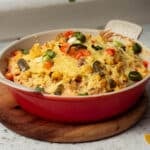 A dish of hot queso dip with corn, jalapenos and spring onions sprinkled on top, with extra melted vegan cheese on top.