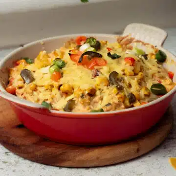 A dish of hot queso dip with corn, jalapenos and spring onions sprinkled on top, with extra melted vegan cheese on top.