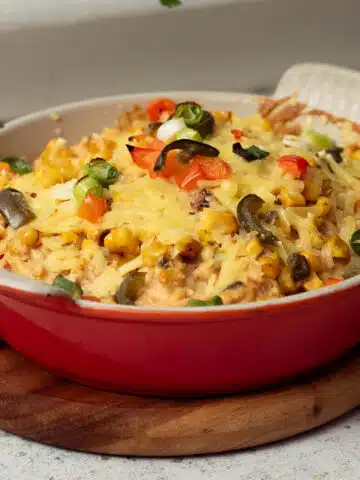 A dish of hot queso dip with corn, jalapenos and spring onions sprinkled on top, with extra melted vegan cheese on top.