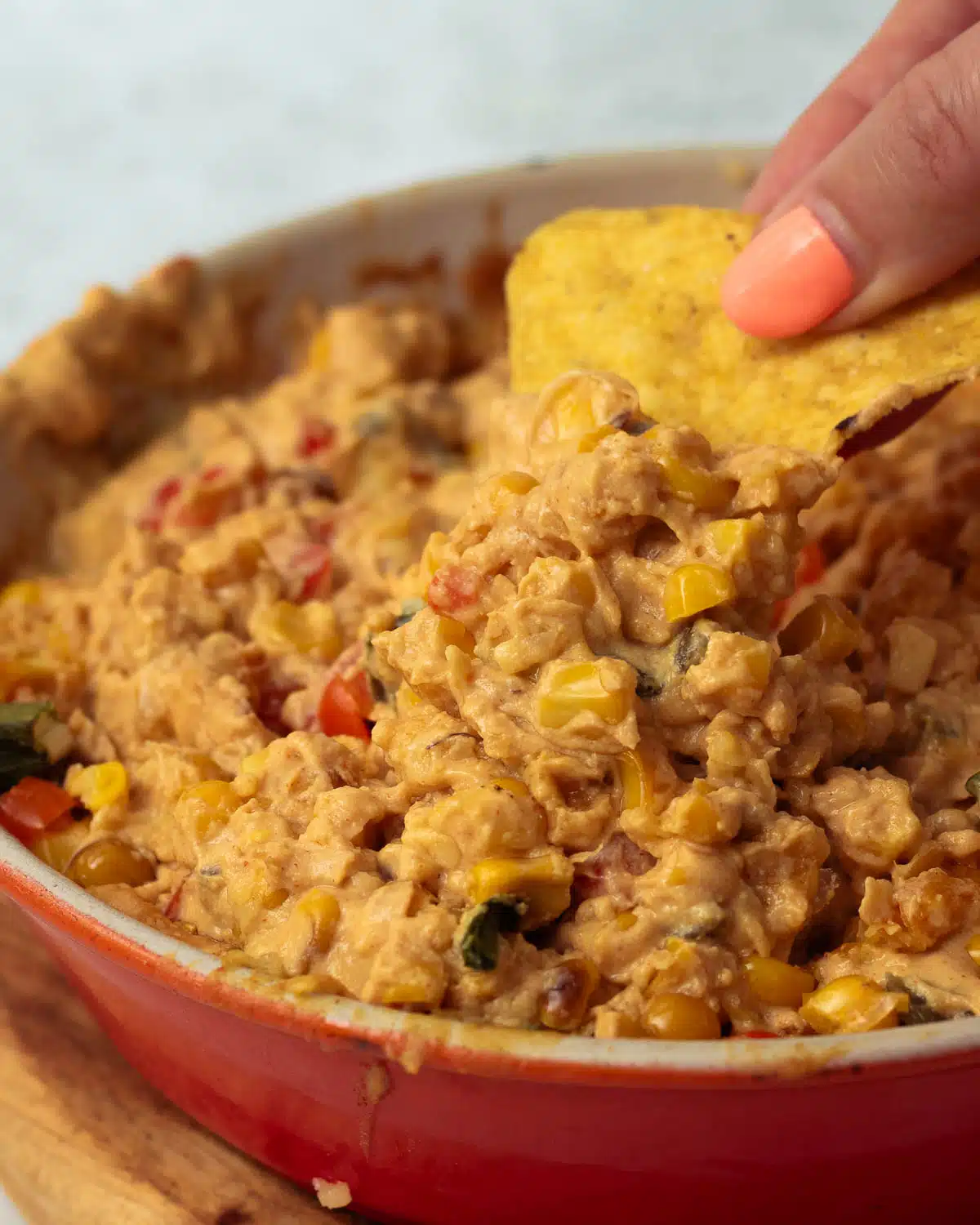 A dish of hot queso dip with corn, jalapenos and spring onions, with a corn chip being dipped into it.