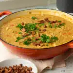 A large pan of vegan split pea and ham soup There are small cubes of vegan faux bacon sprinkled on top of the soup along with some parsley.