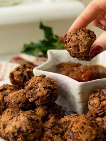 A plate of cranberry bean meatballs with dipping sauce and a hand reaching in to pick one up.
