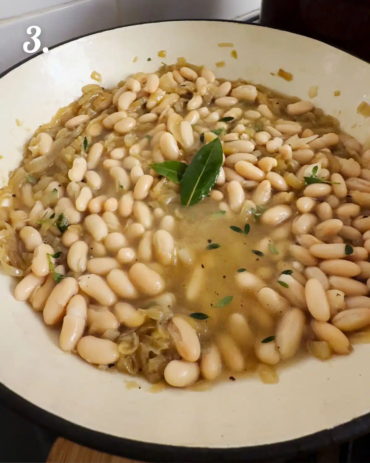 Beans, broth, thyme and bay leaves added to caramelised onions ready to simmer.