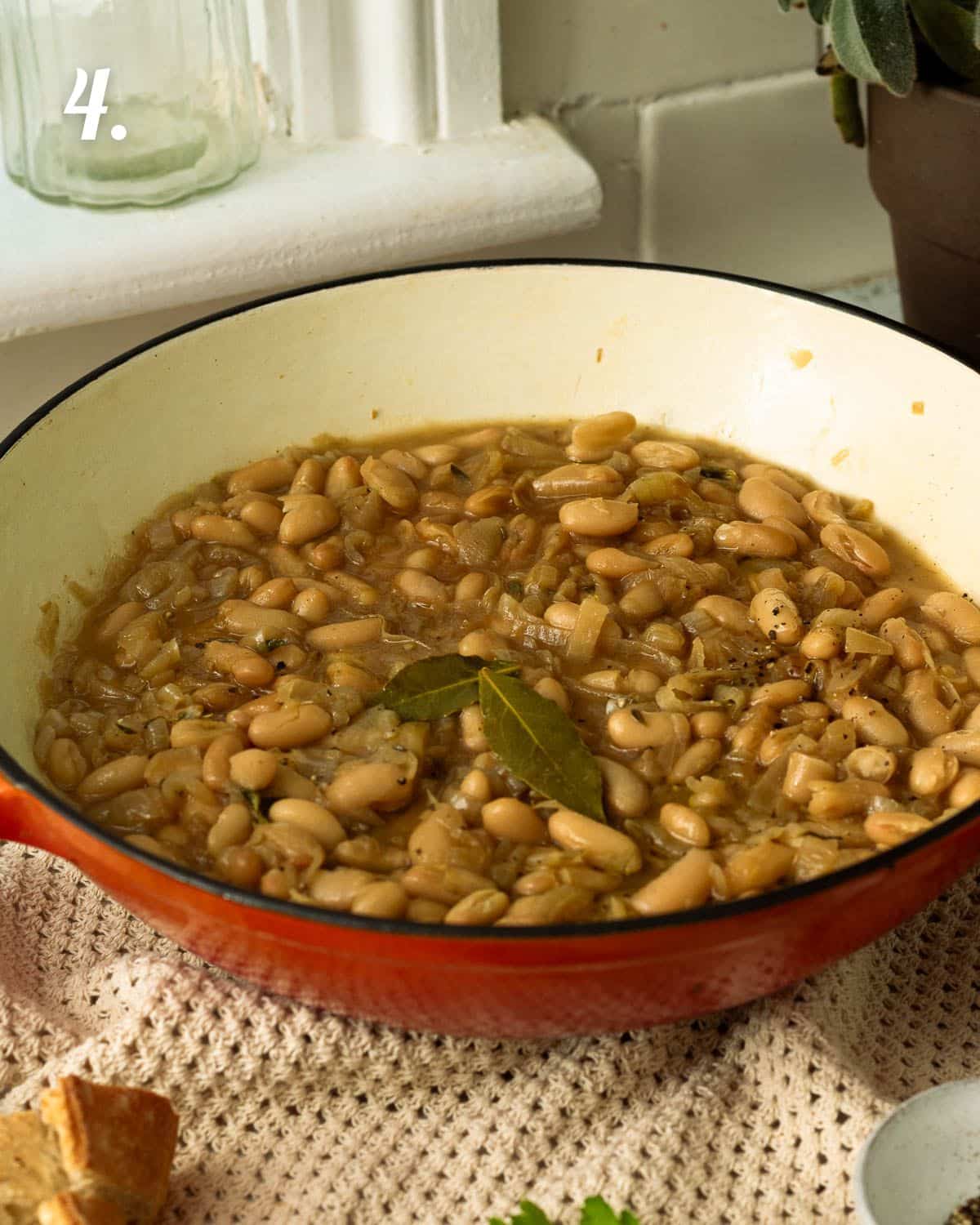 A pan of slowly caramelised onions with white beans ready to eat. There are two bay leaves on top of the beans.