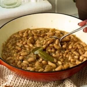 A pan of slowly caramelised onions with white beans. There's a spoon lifting out a spoon of the beans ready to eat.