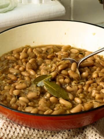 A pan of slowly caramelised onions with white beans. There's a spoon lifting out a spoon of the beans ready to eat.