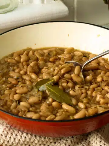 A pan of slowly caramelised onions with white beans. There's a spoon lifting out a spoon of the beans ready to eat.