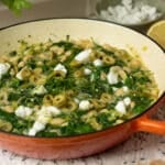 A pan of white beans with spinach, dill and some feta cheese on top ready to eat.
