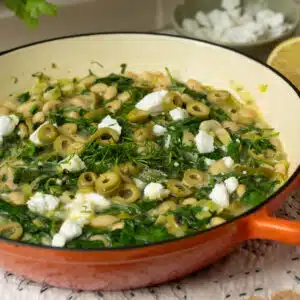 A pan of white beans with spinach, dill and some feta cheese on top ready to eat.