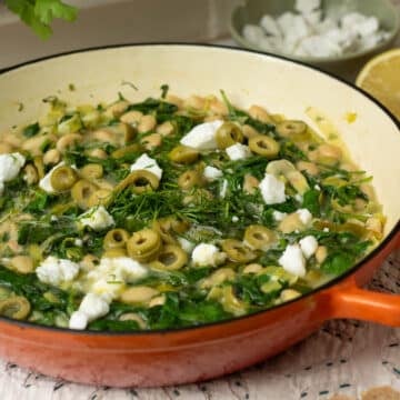 A pan of white beans with spinach, dill and some feta cheese on top ready to eat.