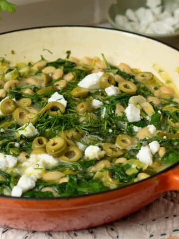 A pan of white beans with spinach, dill and some feta cheese on top ready to eat.