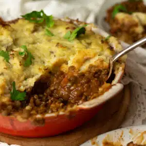 A vegan shepherds pie with a lentil bolognese base with a spoon scooping out the pie onto another plate.