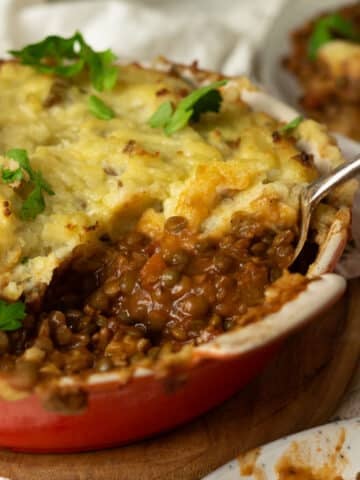 A vegan shepherds pie with a lentil bolognese base with a spoon scooping out the pie onto another plate.