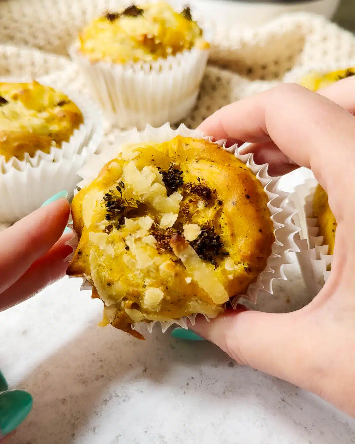 A vegan egg bite ready to eat being held up to the camera. There are other vegan frittata egg bites in the background.