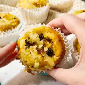 A vegan egg bite ready to eat being held up to the camera. There are other vegan frittata egg bites in the background.