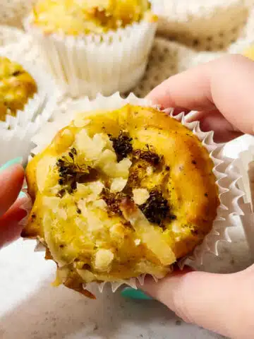 A vegan egg bite ready to eat being held up to the camera. There are other vegan frittata egg bites in the background.
