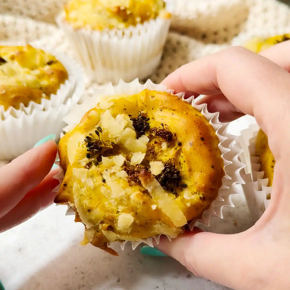 A vegan egg bite ready to eat being held up to the camera. There are other vegan frittata egg bites in the background.