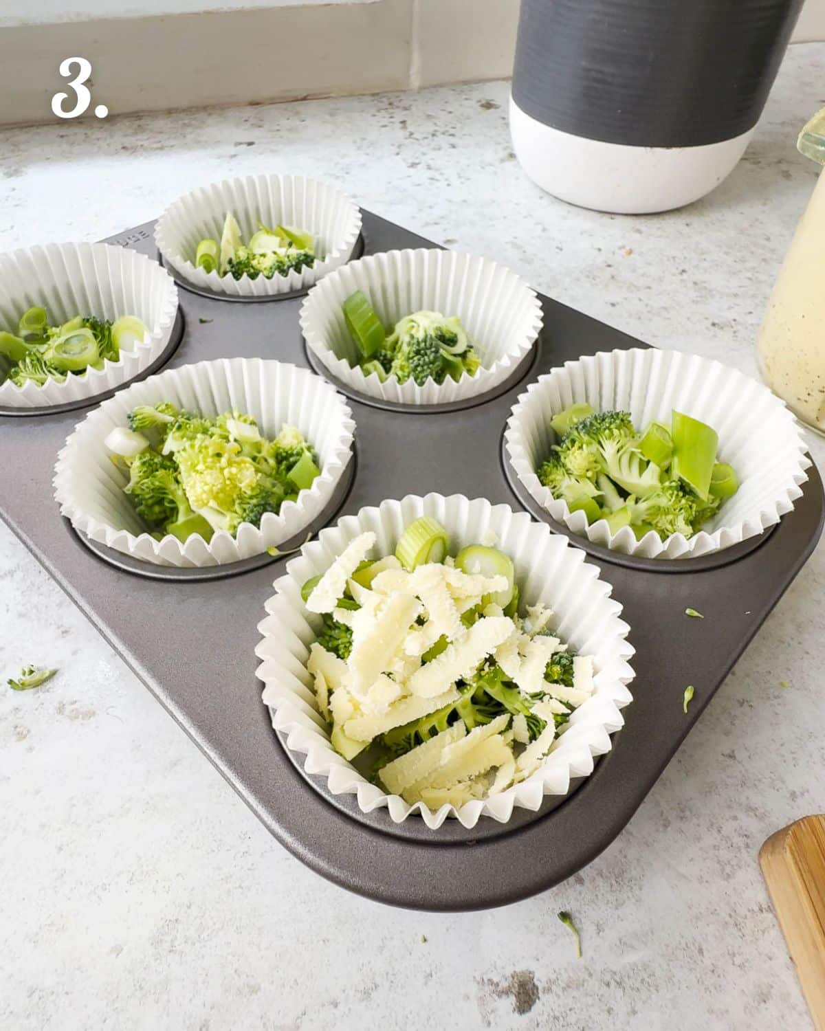 Building the egg bites by starting off with addding the additional ingredients into a muffin pan.