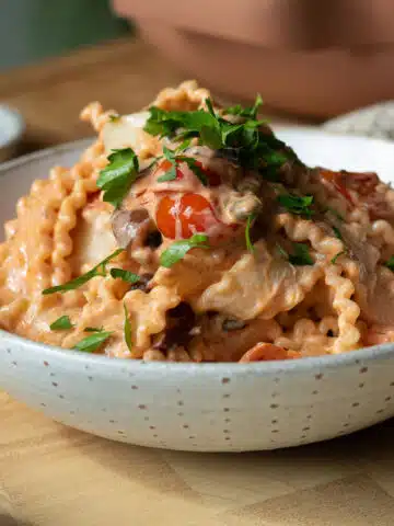 A bowl of creamy tomato puttanesca with some chopped parsley on top.