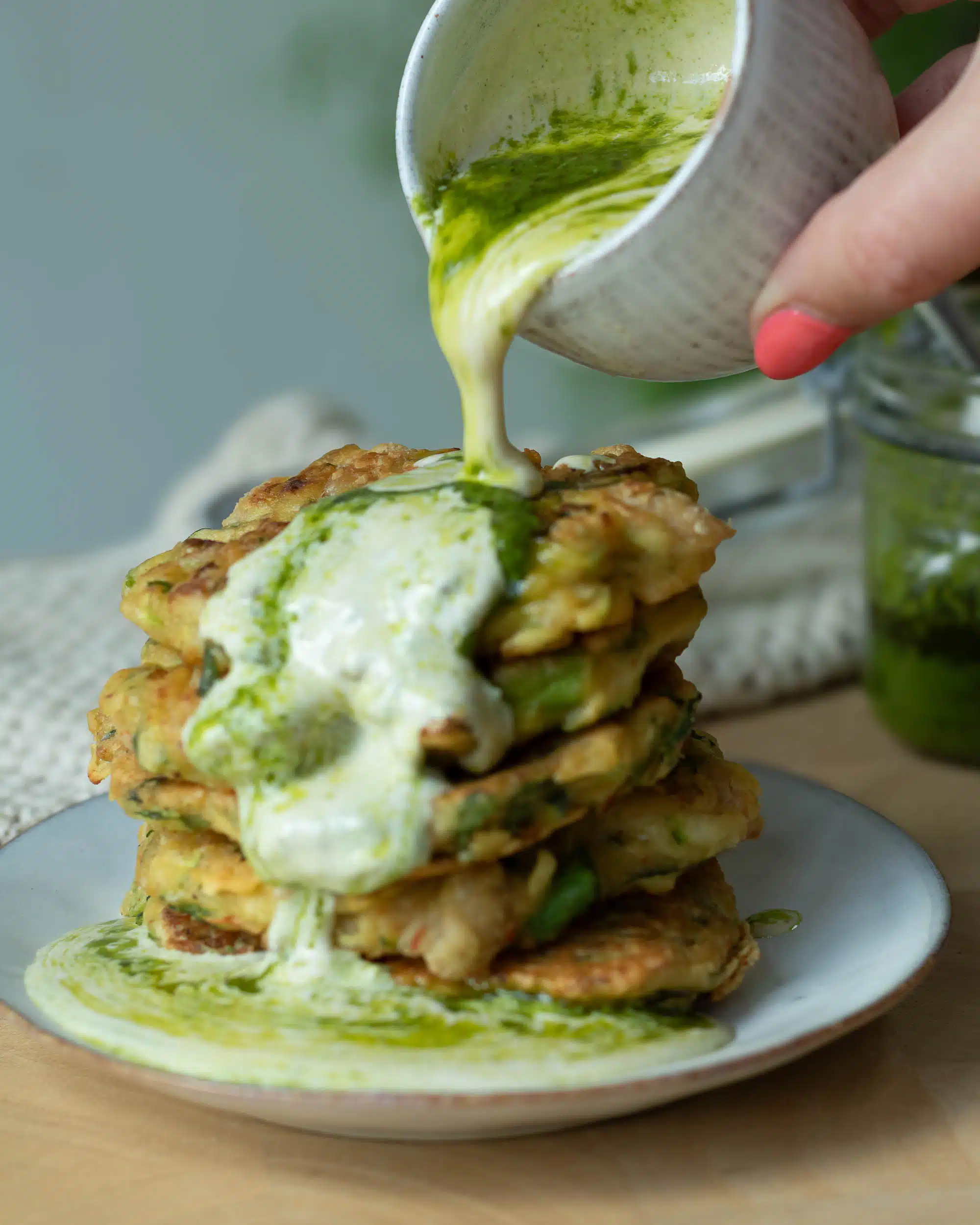 Tahini and herb oil being poured over a stack of veggie fritters.
