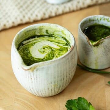 Herb and Tahini Sauce in a pot ready to pour. There is herb oil next to it.