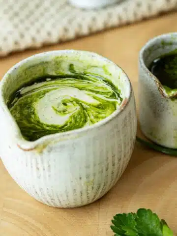 Herb and Tahini Sauce in a pot ready to pour. There is herb oil next to it.