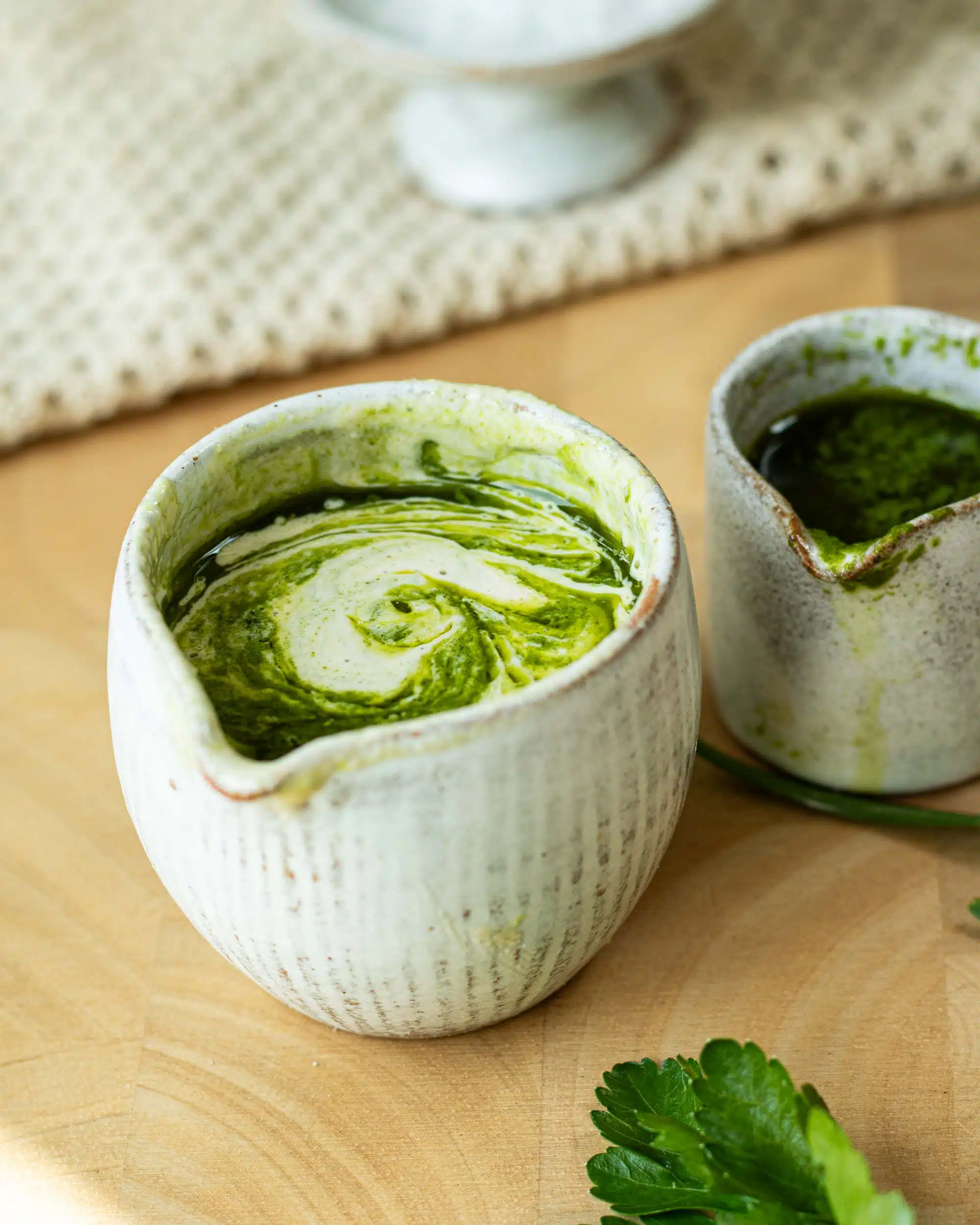 Herb and Tahini Sauce in a pot ready to pour. There is herb oil next to it. 