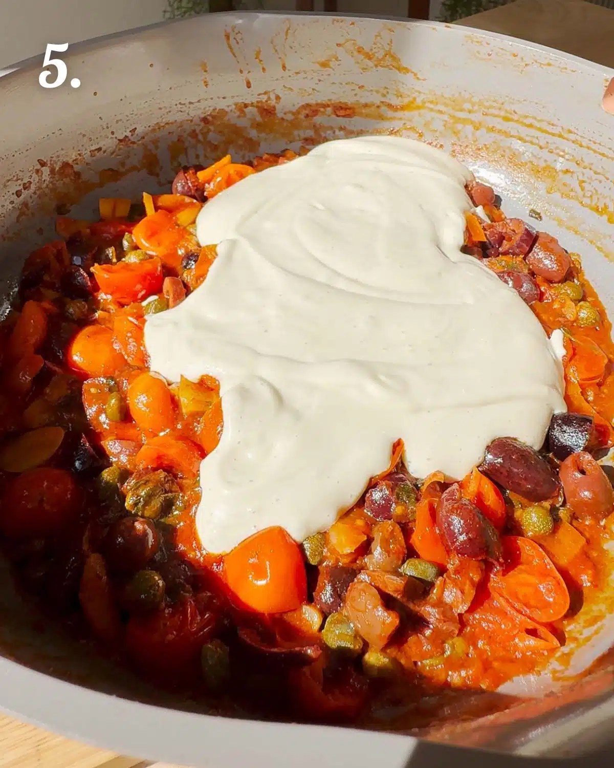 Adding the tofu cream to the tomato puttanesca ready to stir in pasta.