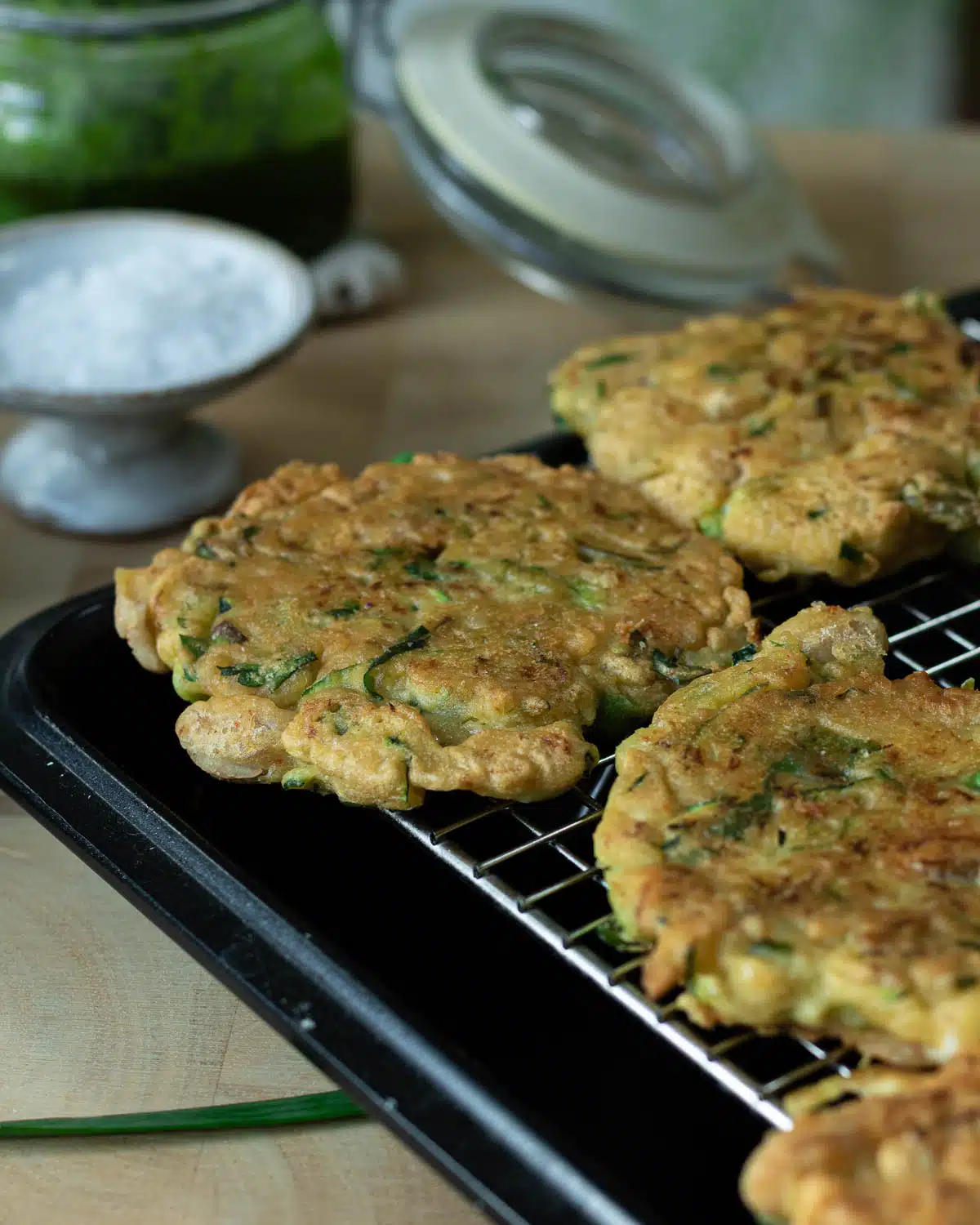 The cooked zucchini white bean fritters sitting on a cookie cooling grid with a pan underneath so they stay dry and crispy.