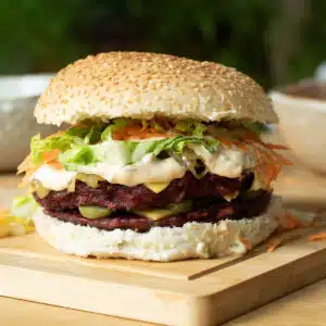 A burger with two lentil and beetroot patties on it, with burger sauce, vegan cheese, carrot and lettuce on it too.