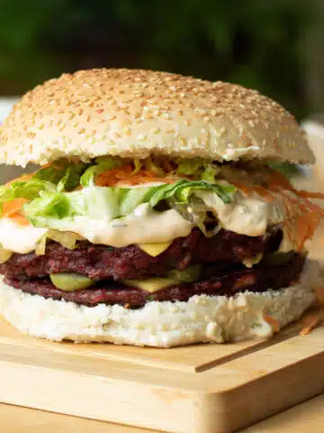 A burger with two lentil and beetroot patties on it, with burger sauce, vegan cheese, carrot and lettuce on it too.