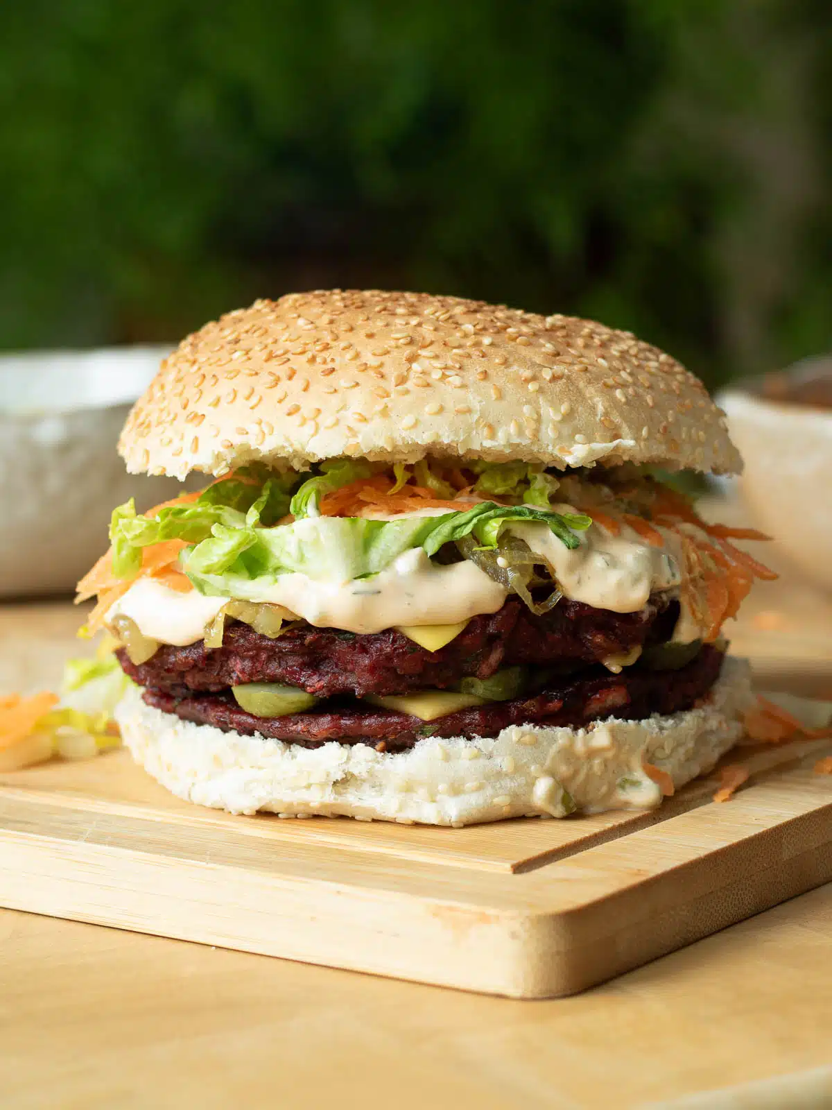 A burger with two lentil and beetroot patties on it, with burger sauce, vegan cheese, carrot and lettuce on it too. 